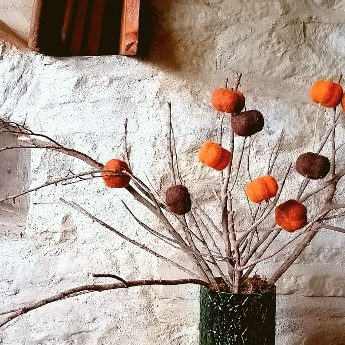 Decorative arrangement with orange and brown pumpkins on branches against a textured wall.