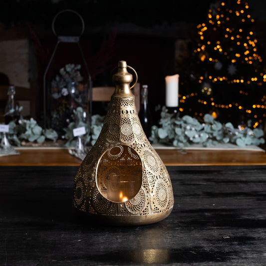 Decorative lantern with intricate patterns on a dark surface, with blurred background of plants and lights.