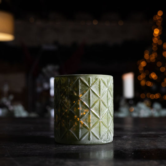 Green textured candle holder on a dark surface with blurred lights in the background
