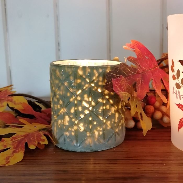 Decorative candle holder with a lit candle on a wooden surface with autumn leaves and berries.