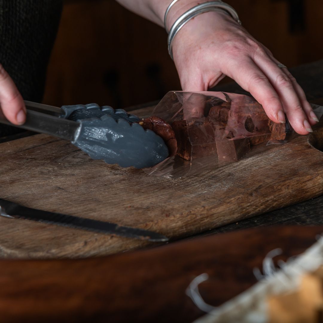 Annabelle using tongs to handle a piece of fudge into a packaging bag on a wooden surface