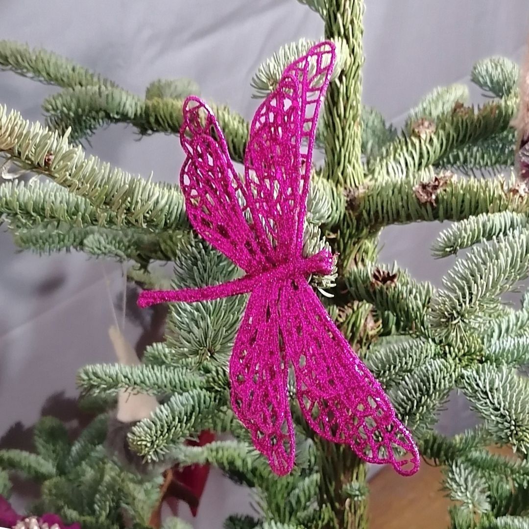 Showing the hot pink glittered butterfly decoration on a Christmas tree with a dark grey background
