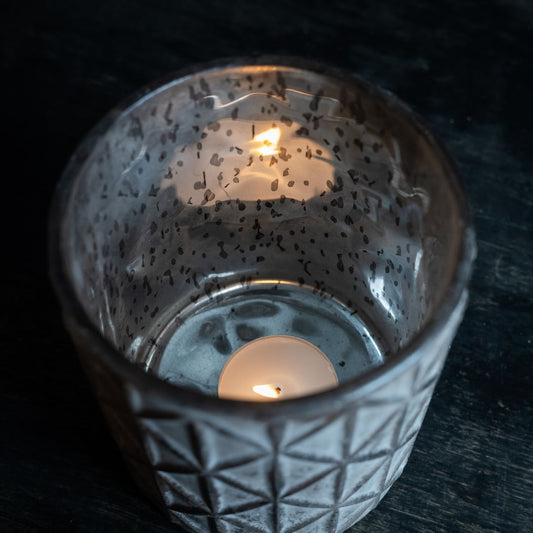 Glass candle holder with a lit candle inside on a dark surface
