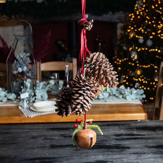 Decorative pine cone ornament with red berries on a dark surface, Christmas tree in the background