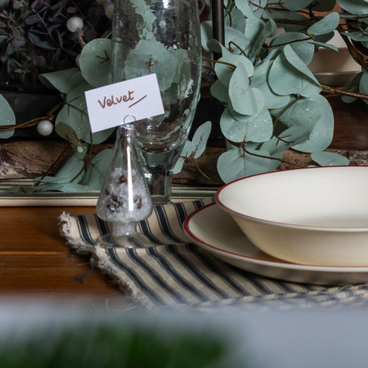 Table setting with a bowl, plate, and glass on a striped tablecloth with decorative plants in the background.