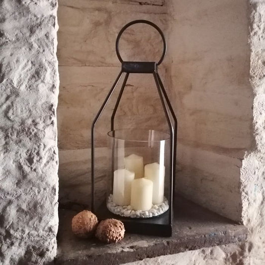 Decorative lantern with candles and pebbles against a stone wall.
