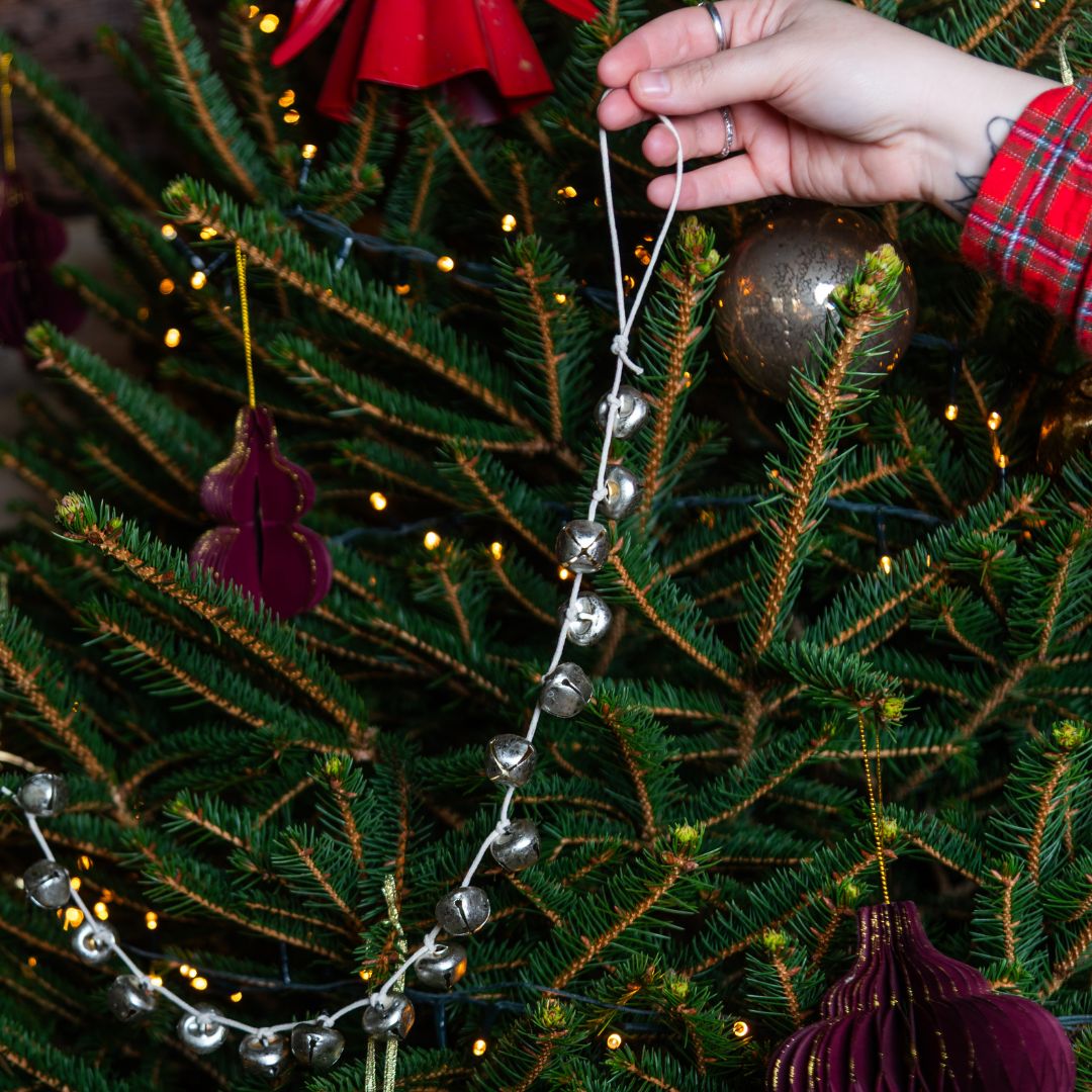 Hand holding the silver metal bell garland against a Christmas tree with it being used as a garland
