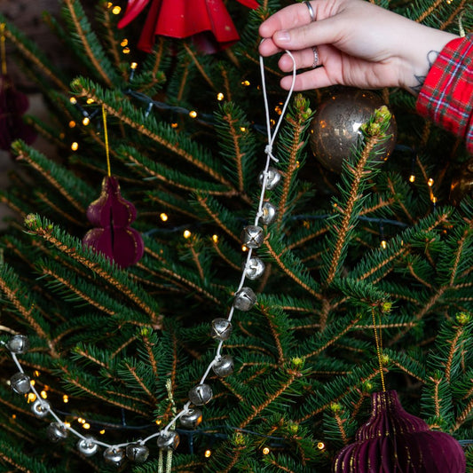 Hand holding the silver metal bell garland against a Christmas tree with it being used as a garland