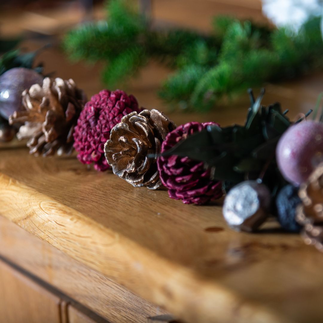 Decorative arrangement of pine cones and burgundy berries on a wooden surface with blurred greenery in the background.