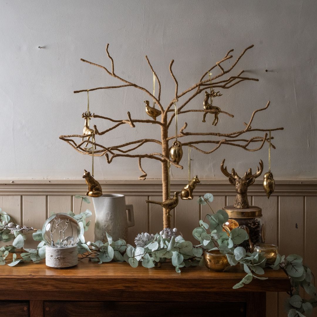 Decorative gold tree with small figurines on a wooden table against a neutral wall.