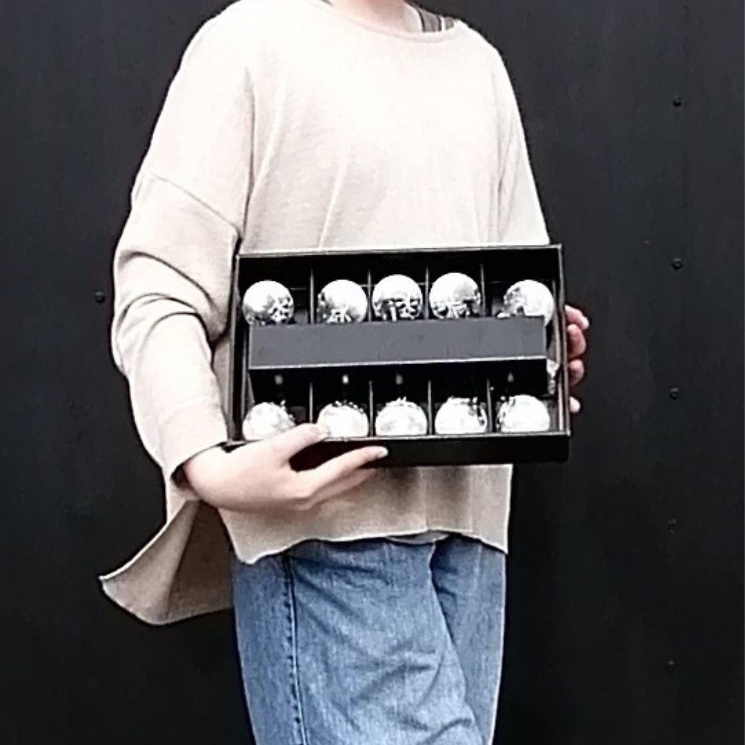 Image showing the size of the box of 10 bauble shaped winter scene battery operated lights in model's hands against a black background