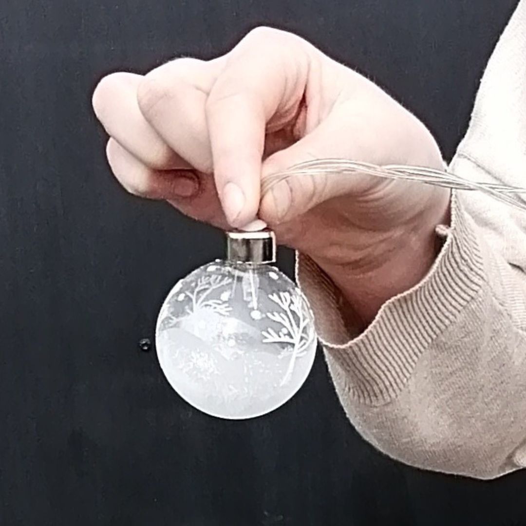 Showing the bauble shaped winter scene battery operated lights in model's hands against a black background