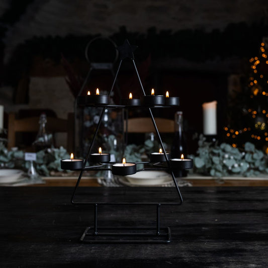 Black tree tea light holder with the 10 tea lights lit against a dark festiv background