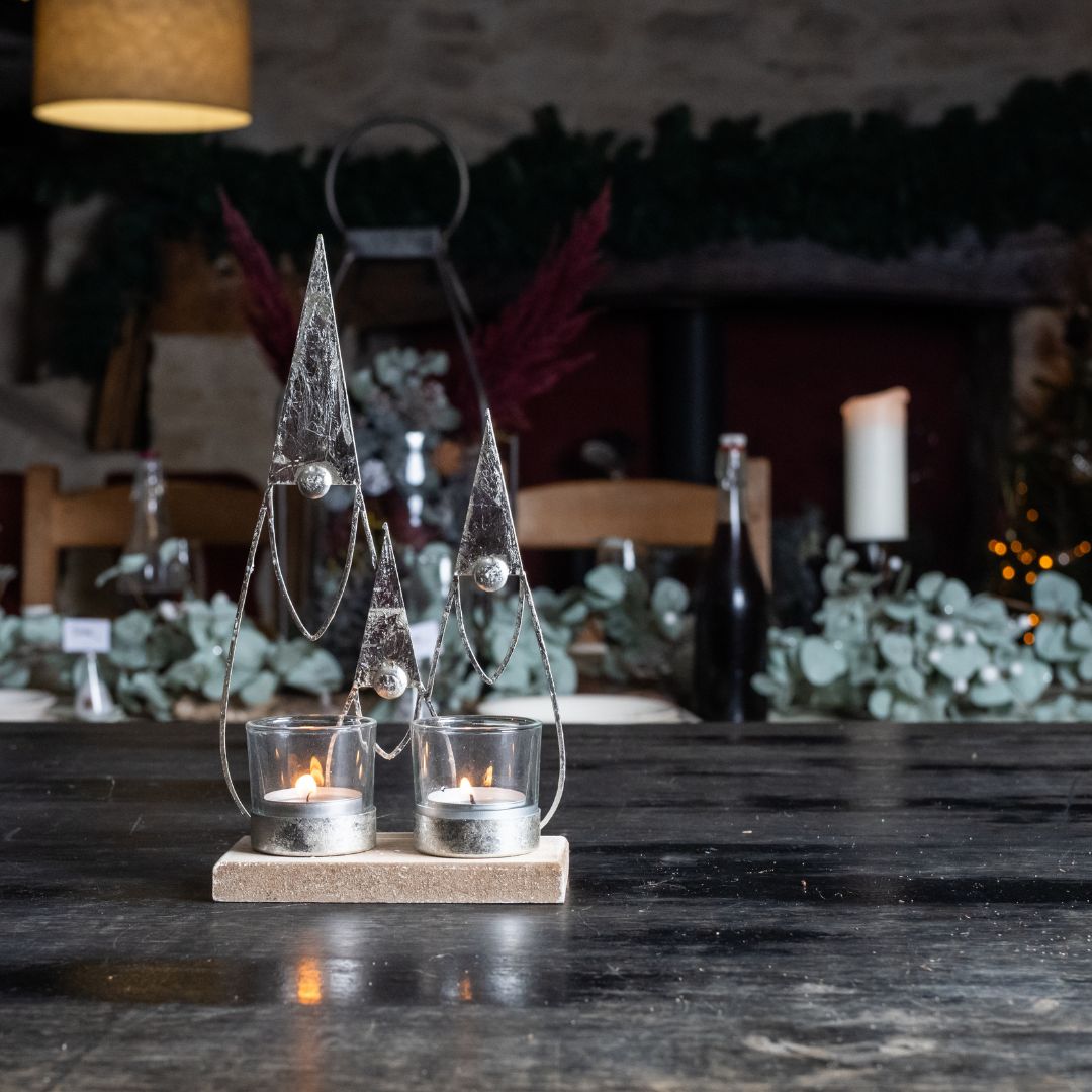 Decorative gonk candle holder with two glass holders on a wooden base in a dimly lit room against a festive background
