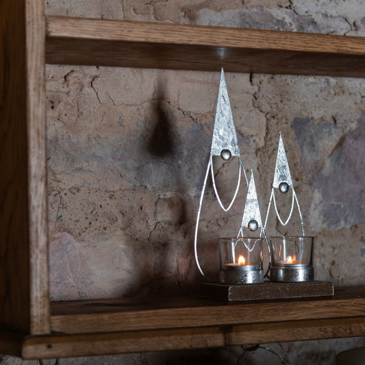 Decorative metal gonks with candles on a wooden shelf against a stone wall.