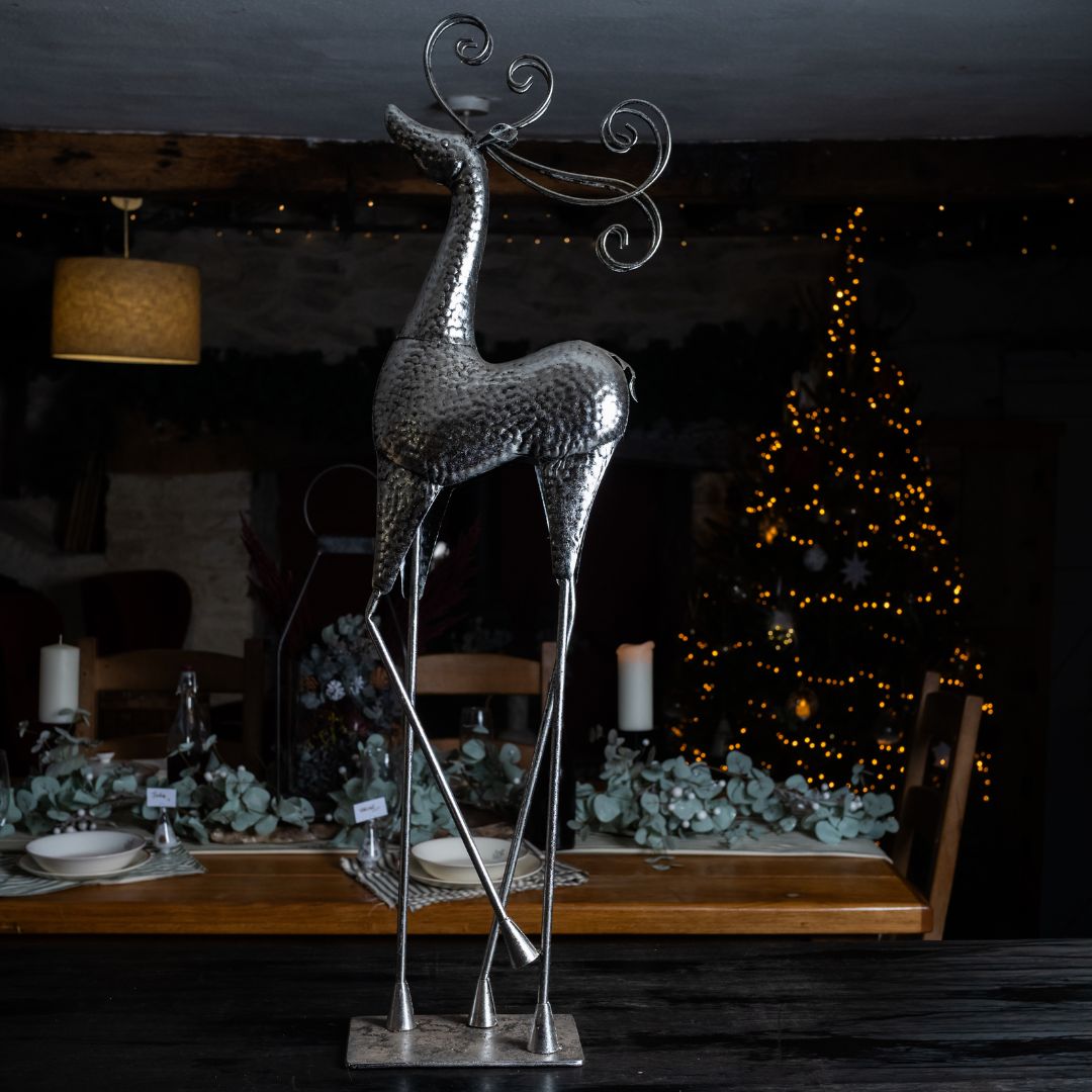 Decorative metal reindeer sculpture on a table with a Christmas tree in the background.