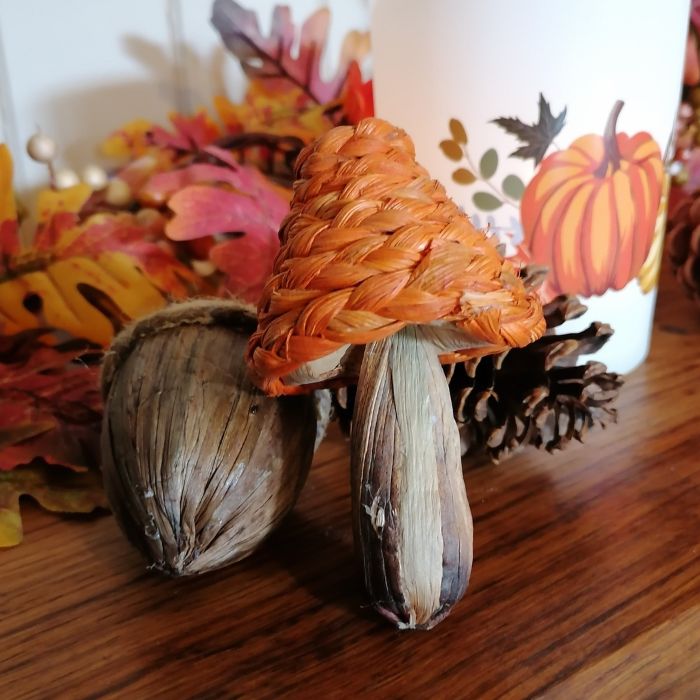 Decorative arrangement with autumn leaves, pinecones, and a candle featuring pumpkin design on a wooden surface.