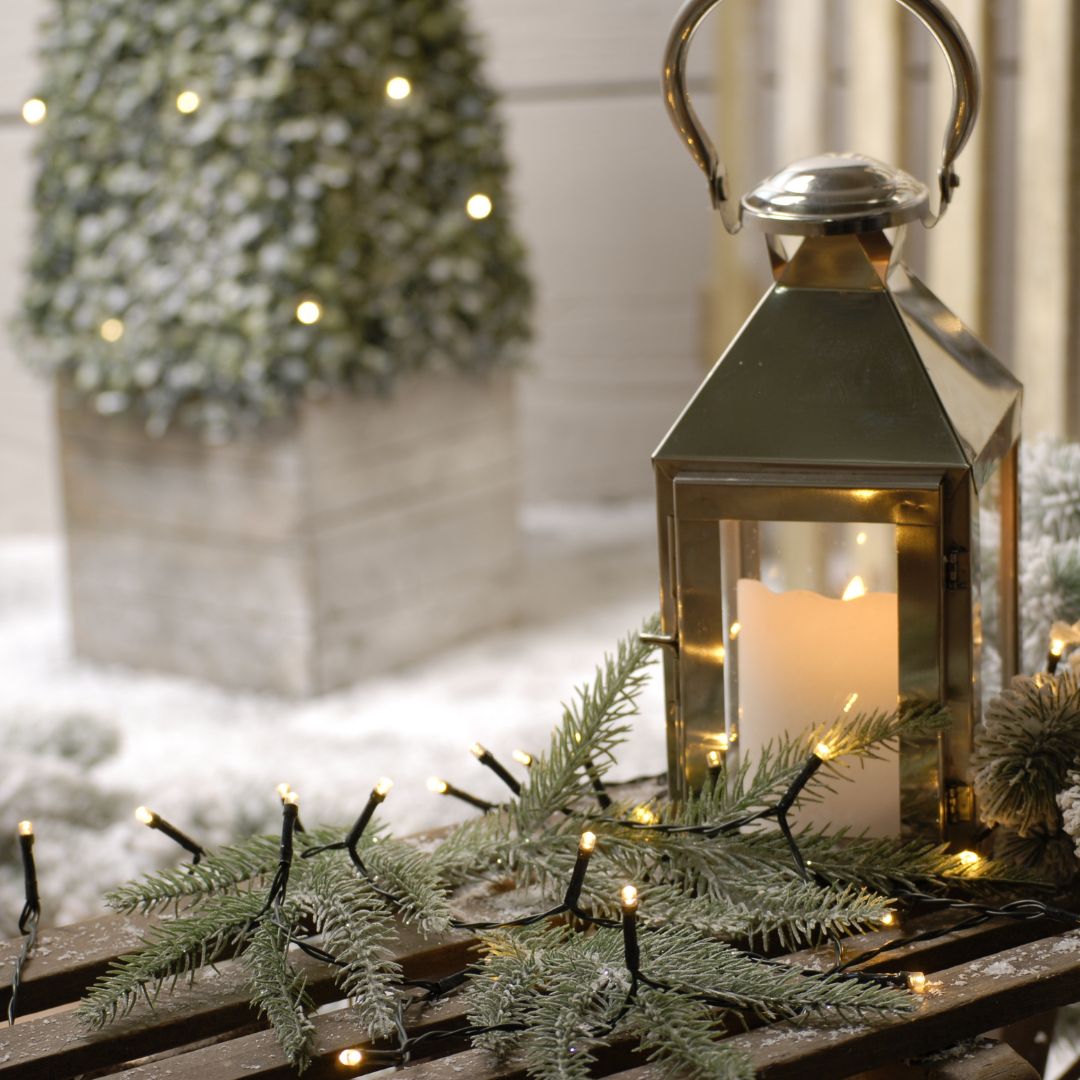 A set of LED battery operated lights with green wires, displayed alongside a lantern and decorative foliage, indicating their use for festive decoration.