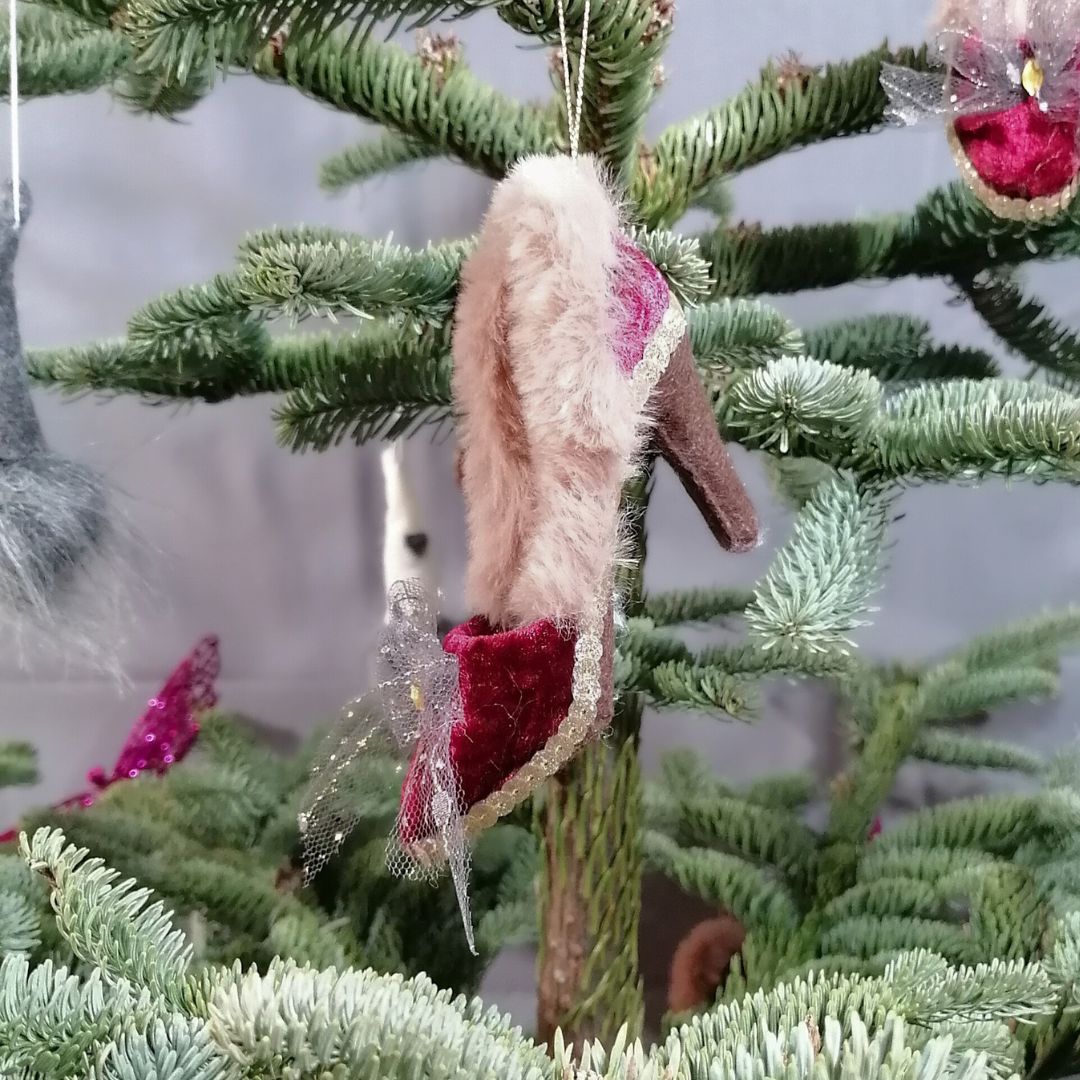 Image of a burgundy velvet shoe hanging decoration on a Christmas tree with a grey background