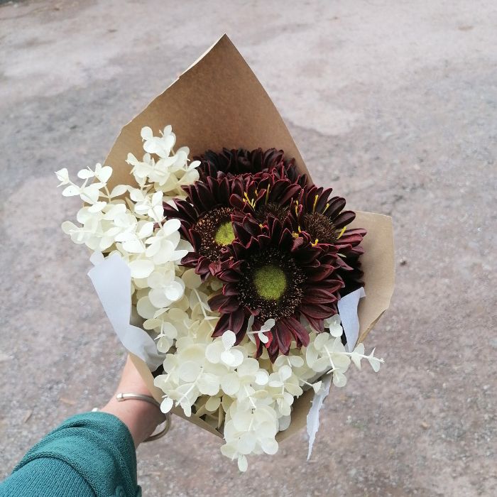 Bouquet of flowers wrapped in brown paper held by a person with a blurred background