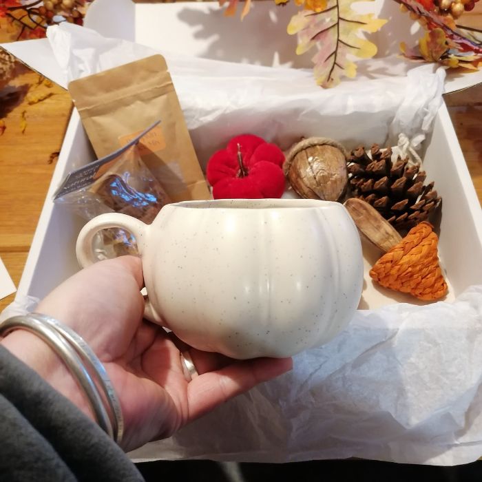 Hand holding a white ceramic mug with autumn-themed items in the background