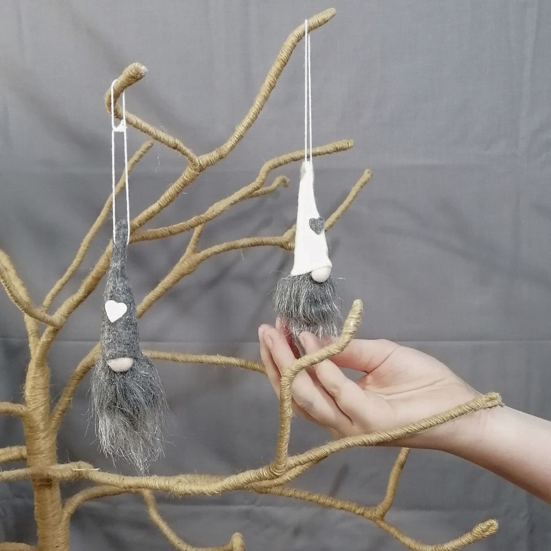 Showing one of each of the grey and white gonk hanging decorations on a branch tree with a model's hand to show the approximate size