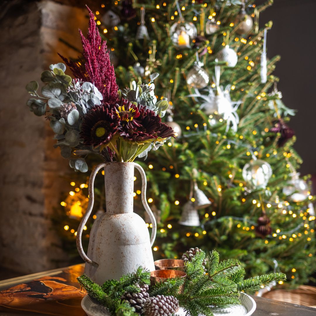 Decorative arrangement with a vase of flowers in front of a Christmas tree.
