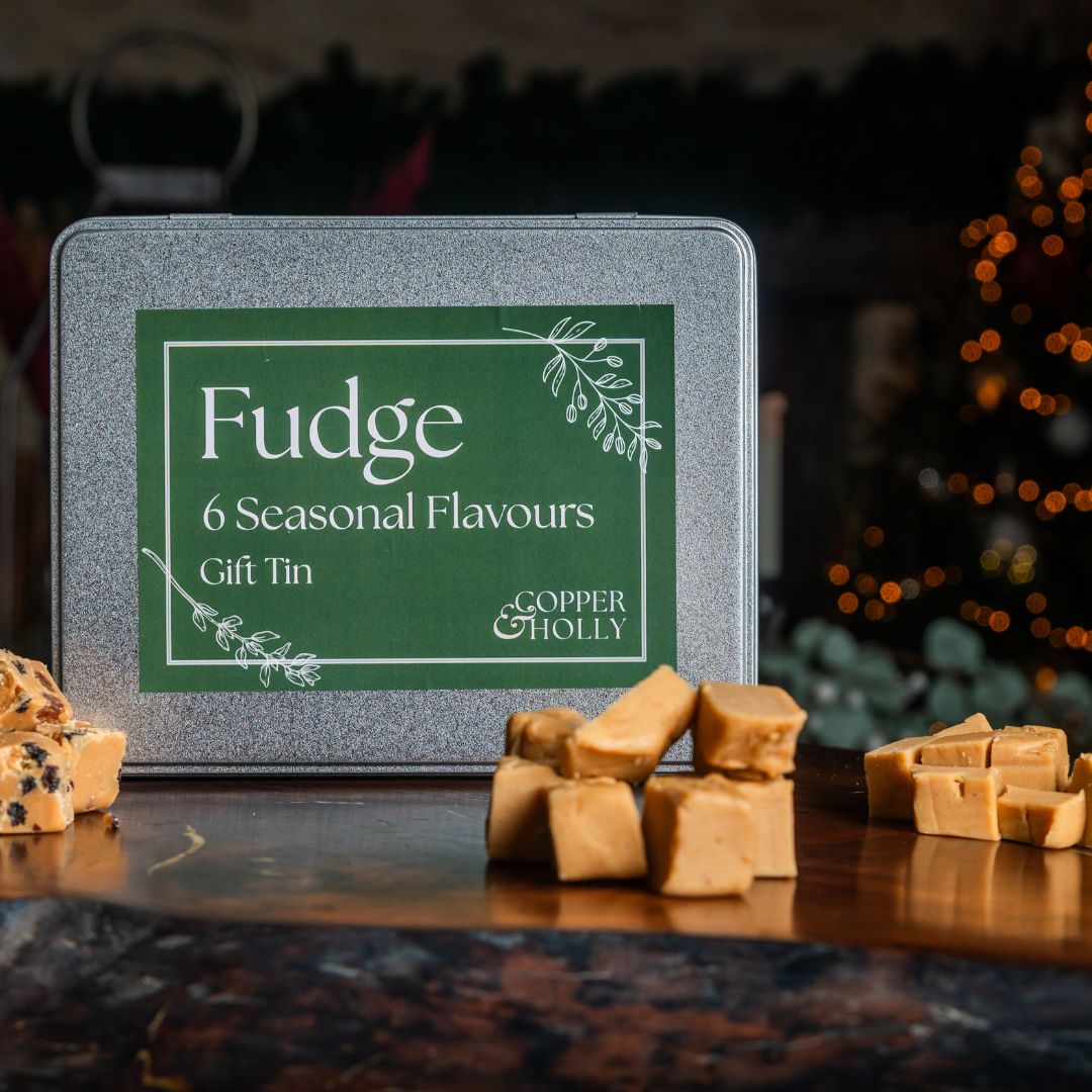 Fudge gift tin with 6 seasonal flavours on a wooden surface, Christmas tree in the background