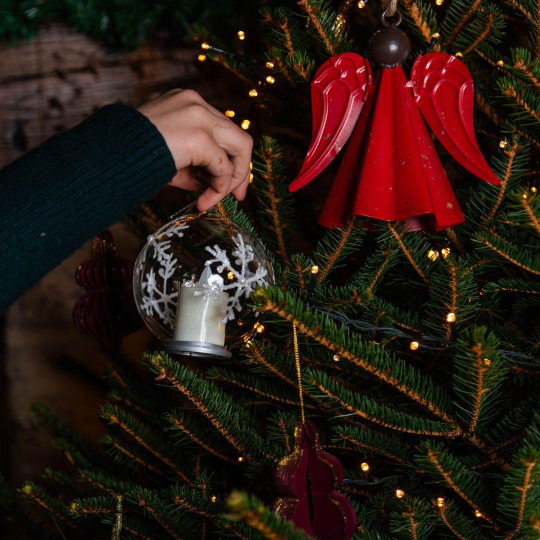 Clear glass LED bauble being put on Christmas tree
