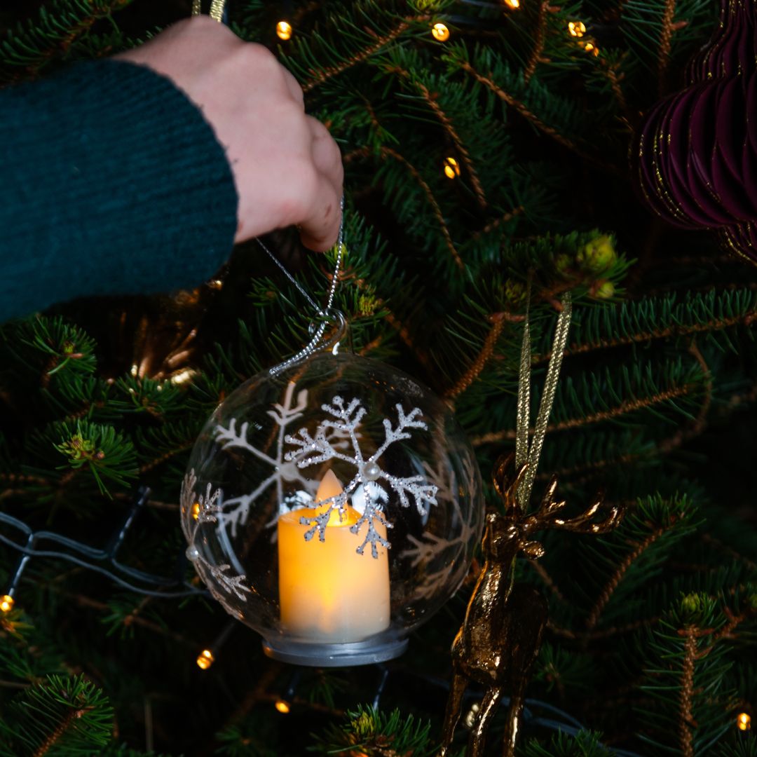 Clear glass LED bauble with candle lit being put on Christmas tree