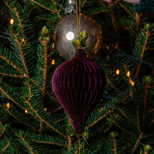 Decorative burgundy ornament hanging on a Christmas tree with lights.