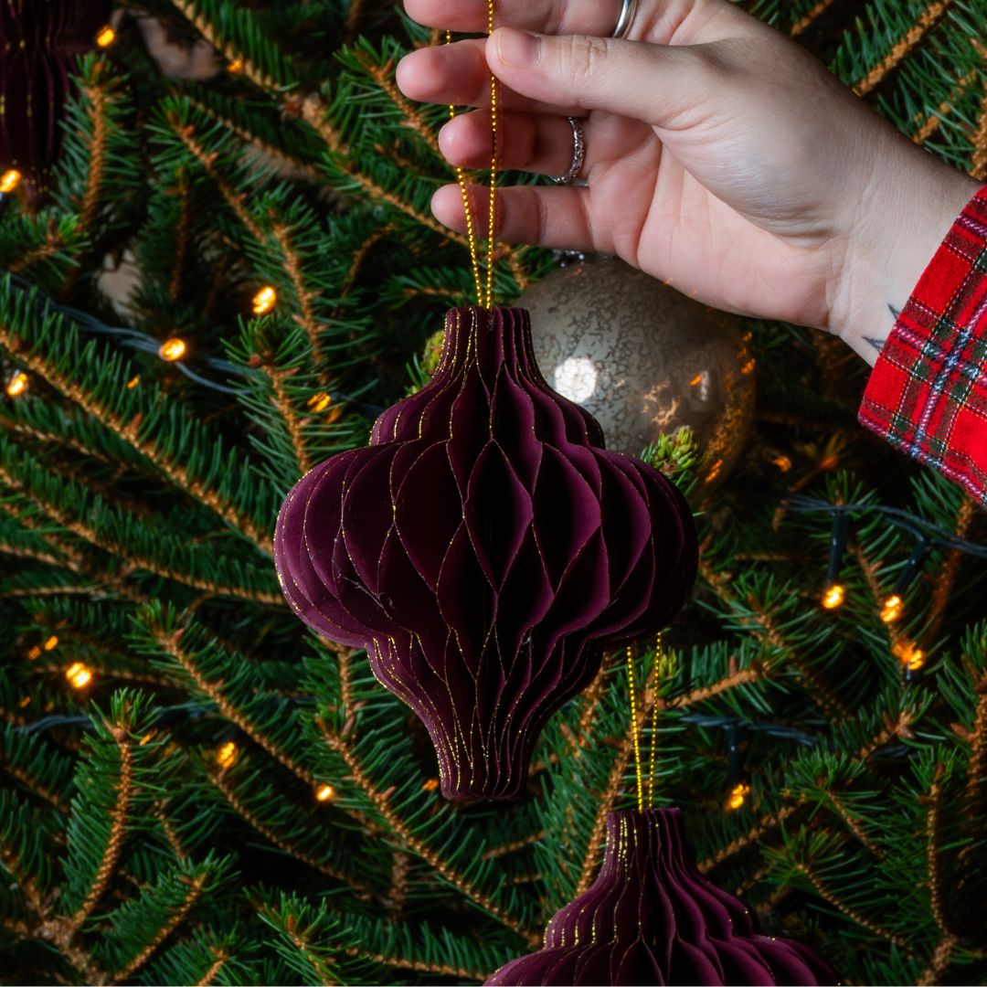 Hand holding a burgundy ornament against a Christmas tree background
