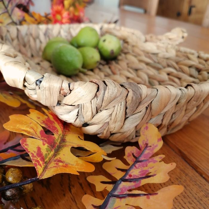 Woven basket with green walnuts on a wooden surface with autumn leaves.