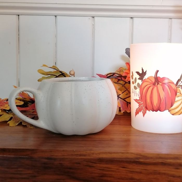 White ceramic pumpkin mug and candle with pumpkin design on a wooden surface.