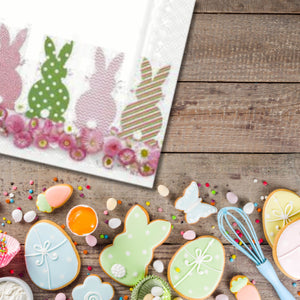 Daisy Day paper napkins sitting on a wooden background with a border at the bottom of easter cookies and small eggs