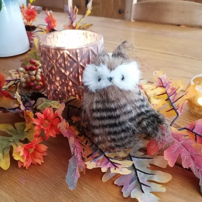 Plush owl toy on a decorative table with flowers and candles