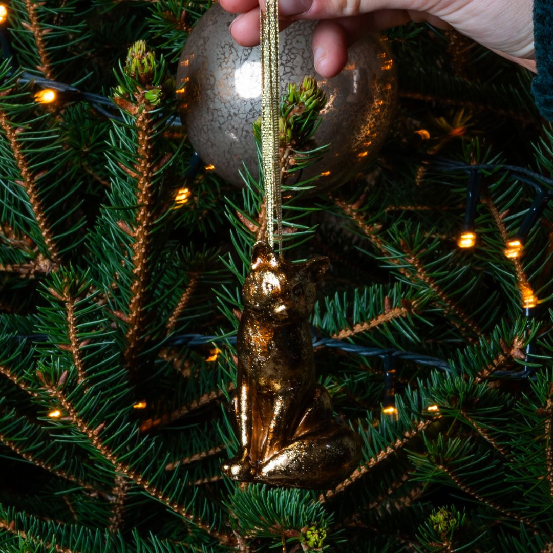 Gold Christmas fox ornament being hung on a tree branch with lights.