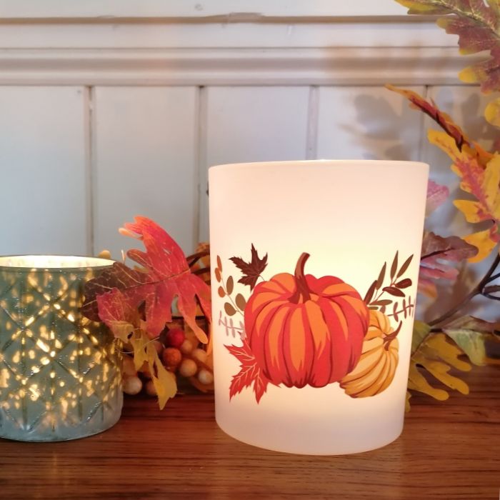 Decorative candle holder with pumpkin design on a wooden surface with fall leaves and berries.