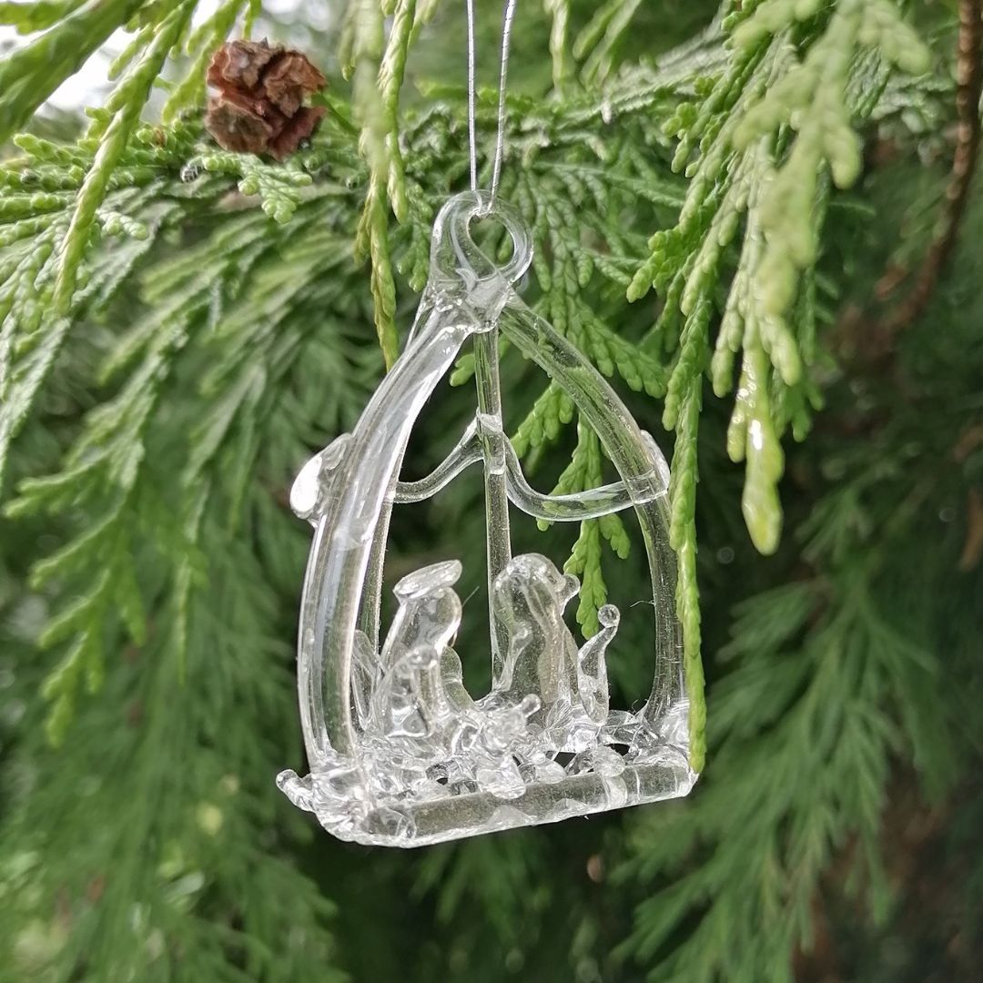 Clear glass nativity scene ornament hanging on a green tree branch.