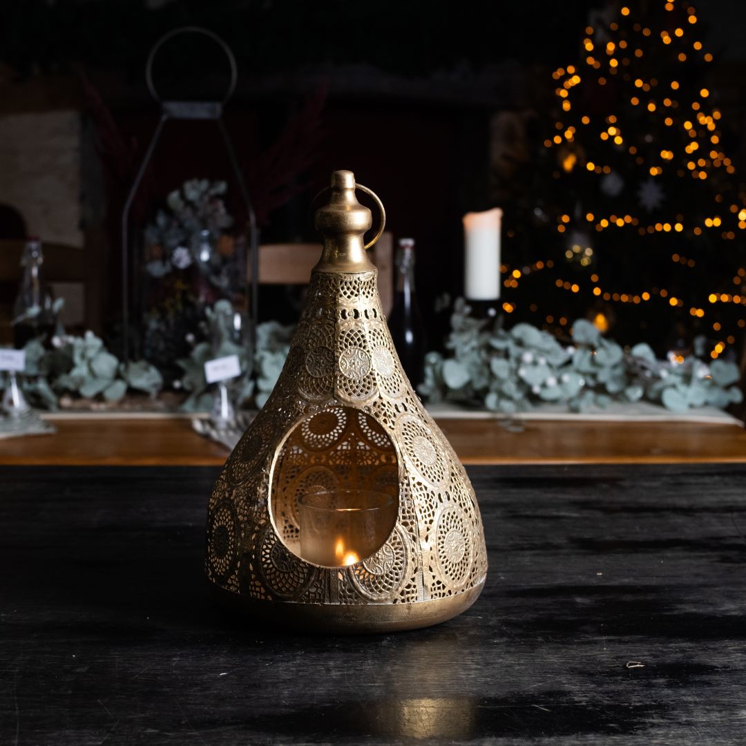 Decorative lantern with intricate patterns on a dark surface, with blurred background of plants and lights.