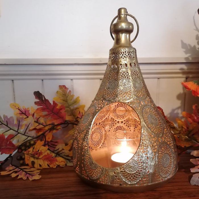 Decorative gold lantern with a candle inside, placed on a surface with autumn leaves in the background.