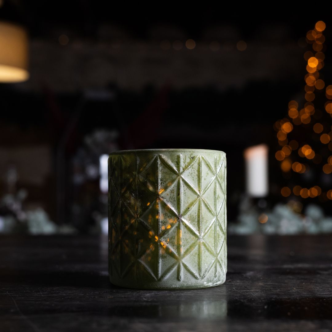 Green textured candle holder on a dark surface with blurred lights in the background