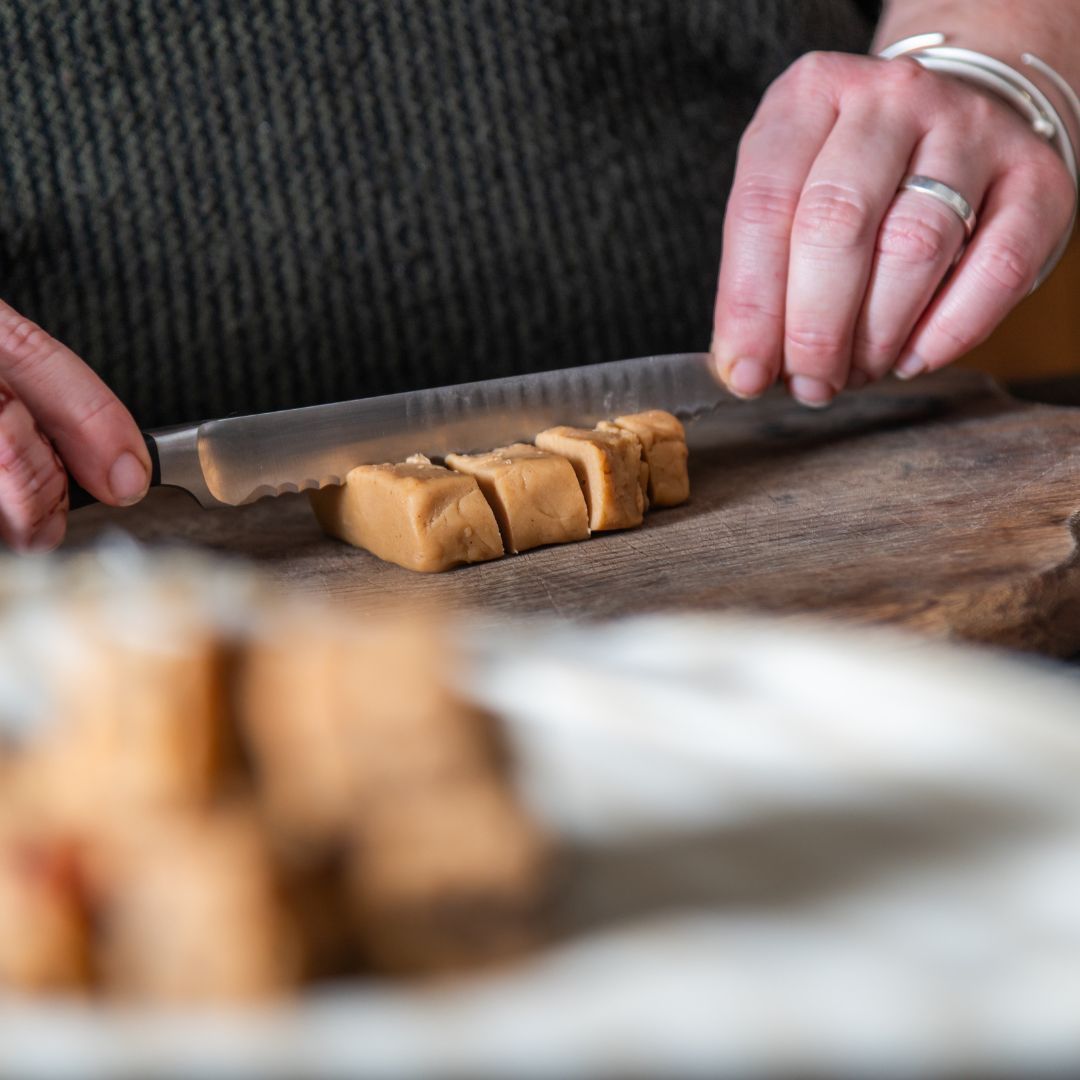 Annabelle cutting fudge into cubes on a wooden board with a knife.