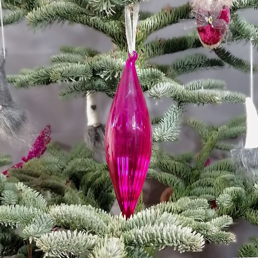An image showing a hot pink glass hanging decoration on the Christmas tree, with a dark grey background 