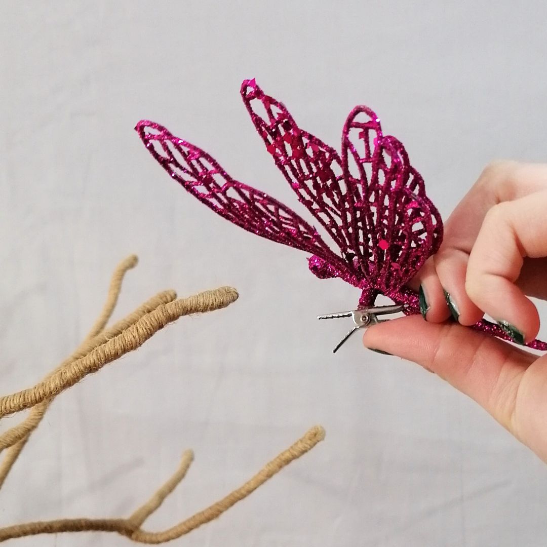 Image showing a close up of the clip open in a model's fingers of the hot pink glittered butterfly clip on decoration