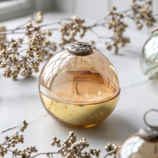 Round glass bauble container with a glass lid on a light surface with dried flowers.