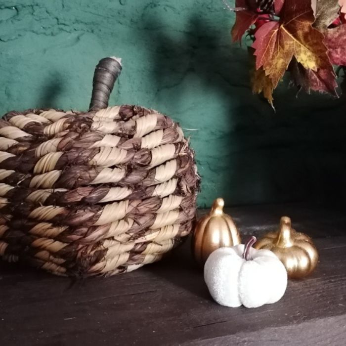 Woven pumpkin, white pumpkin, and gold pumpkins on a dark surface with a green background