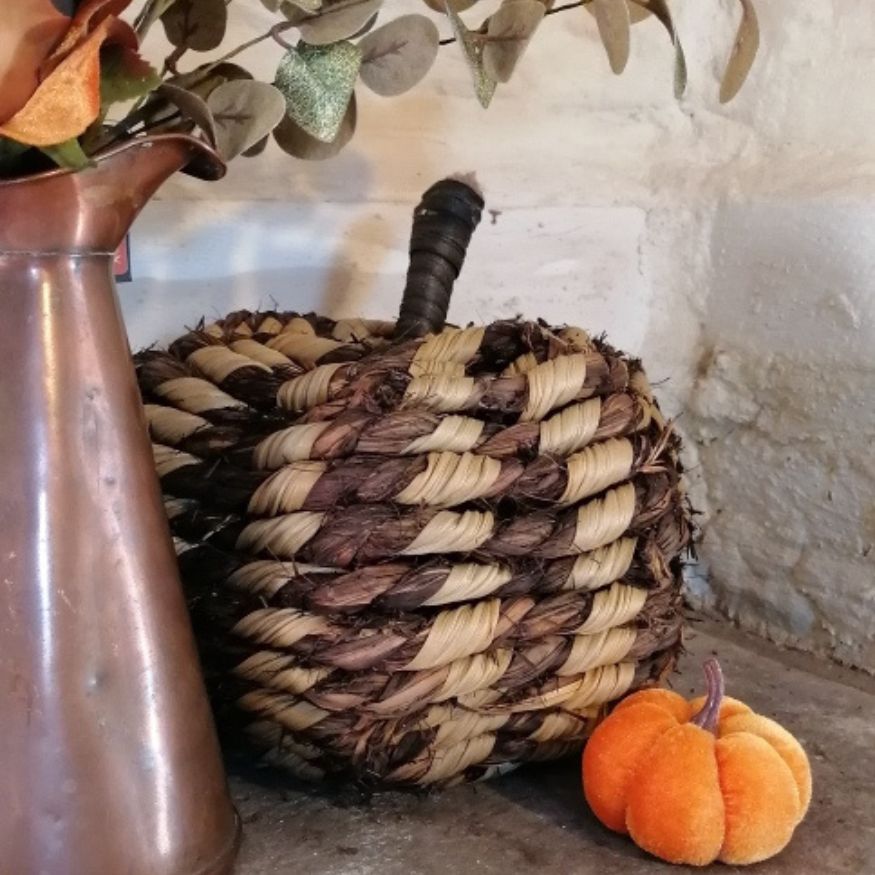 Woven pumpkin with a copper pitcher and small pumpkin on a stone surface.