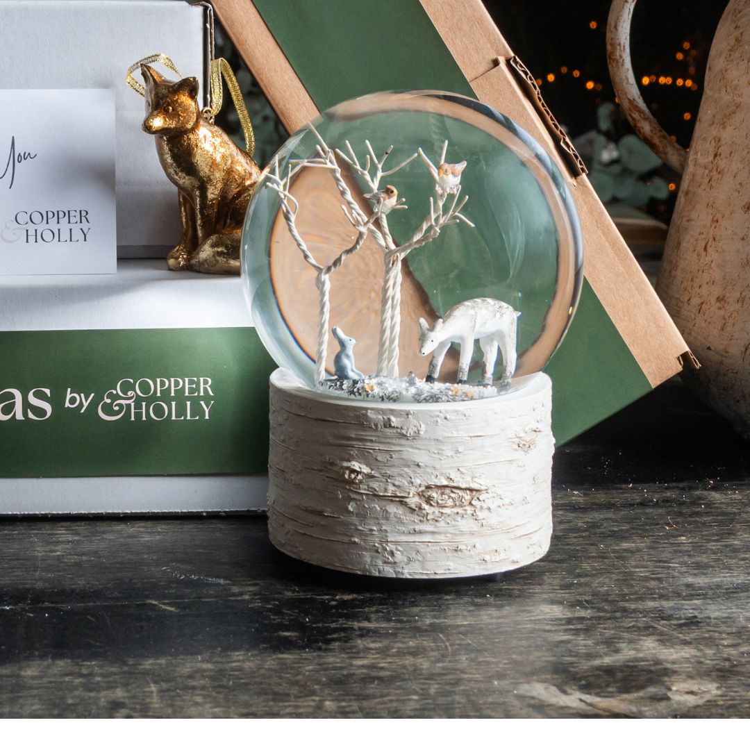 Decorative snow globe with animals on a wooden surface, featuring 'Copper & Holly' branding.