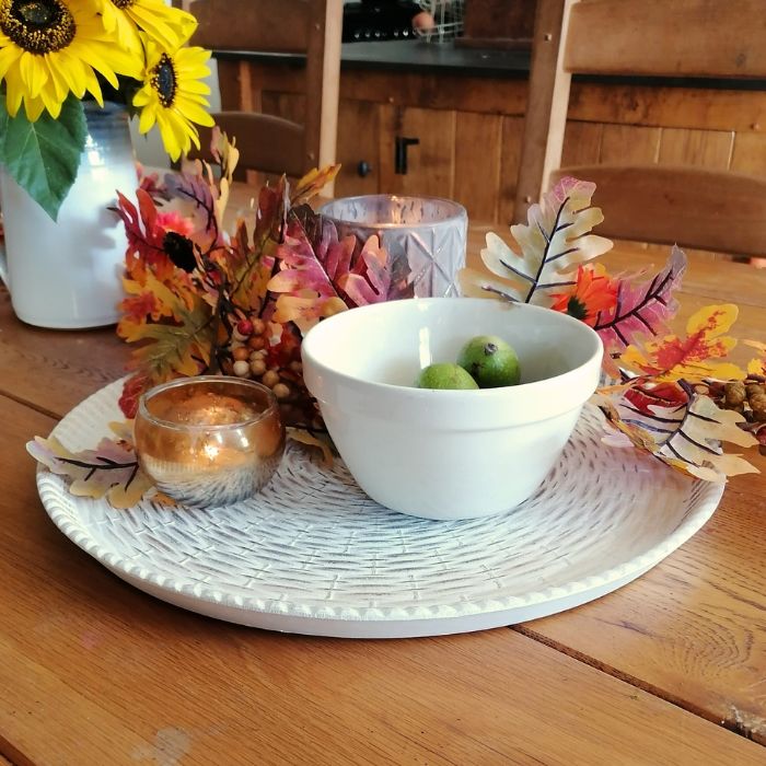 Decorative table setting with a bowl, candles, and fall-themed decorations on a wooden table.